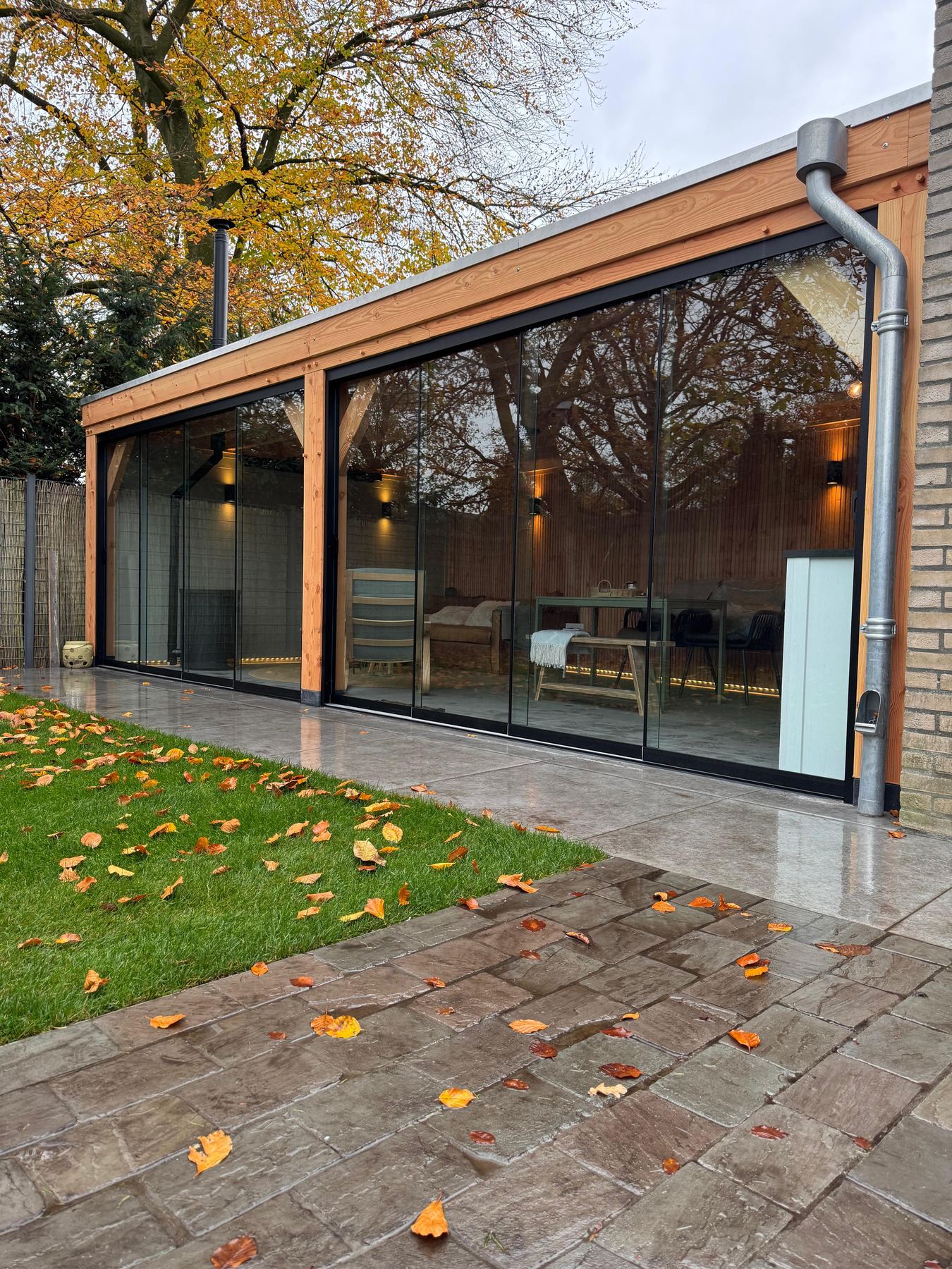 Tuinkamer met glazen pui en verlichting, met herfstbladeren op het terras