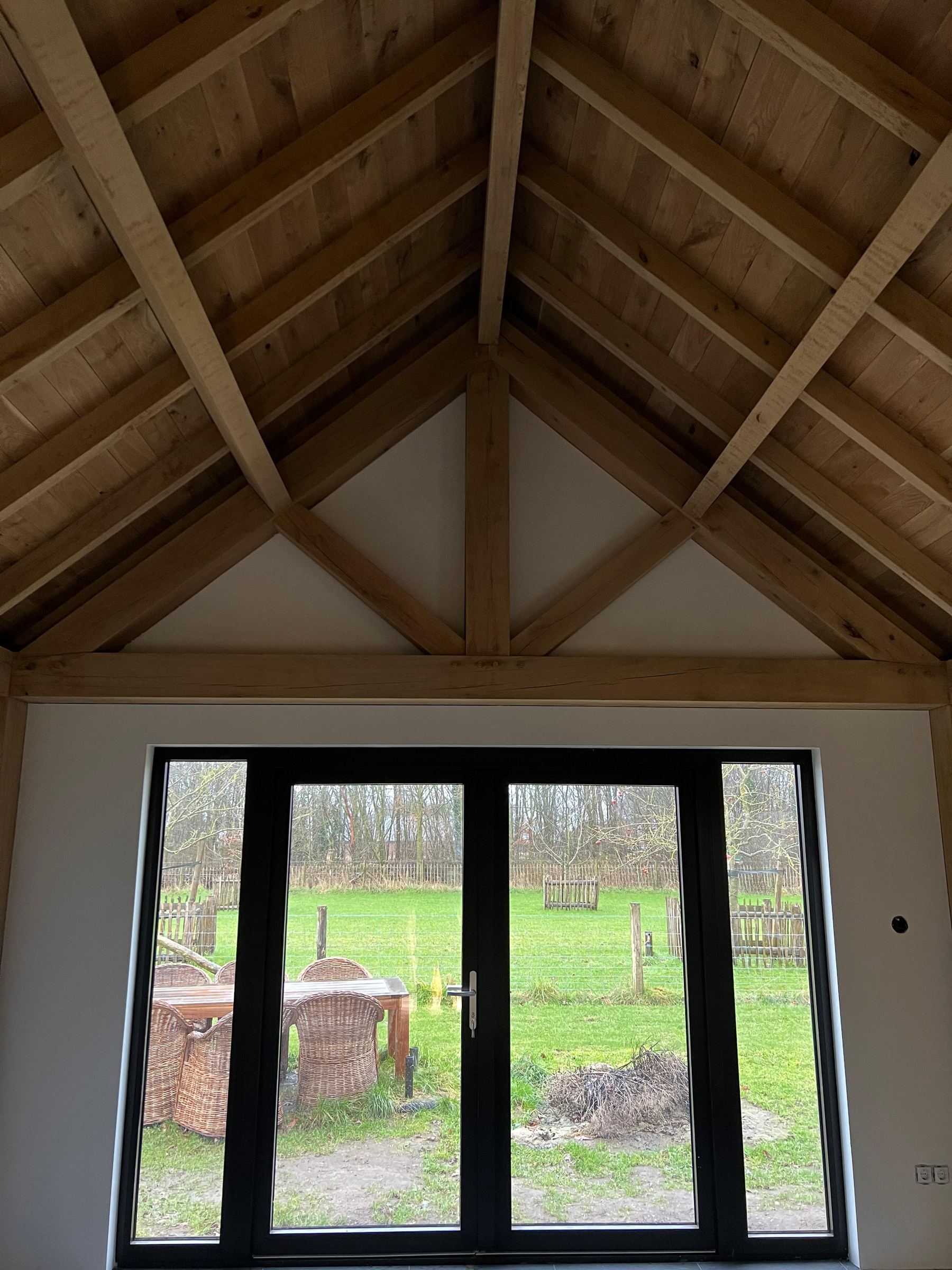 Uitzicht door een zwart kozijn op het weiland achter het gebouw