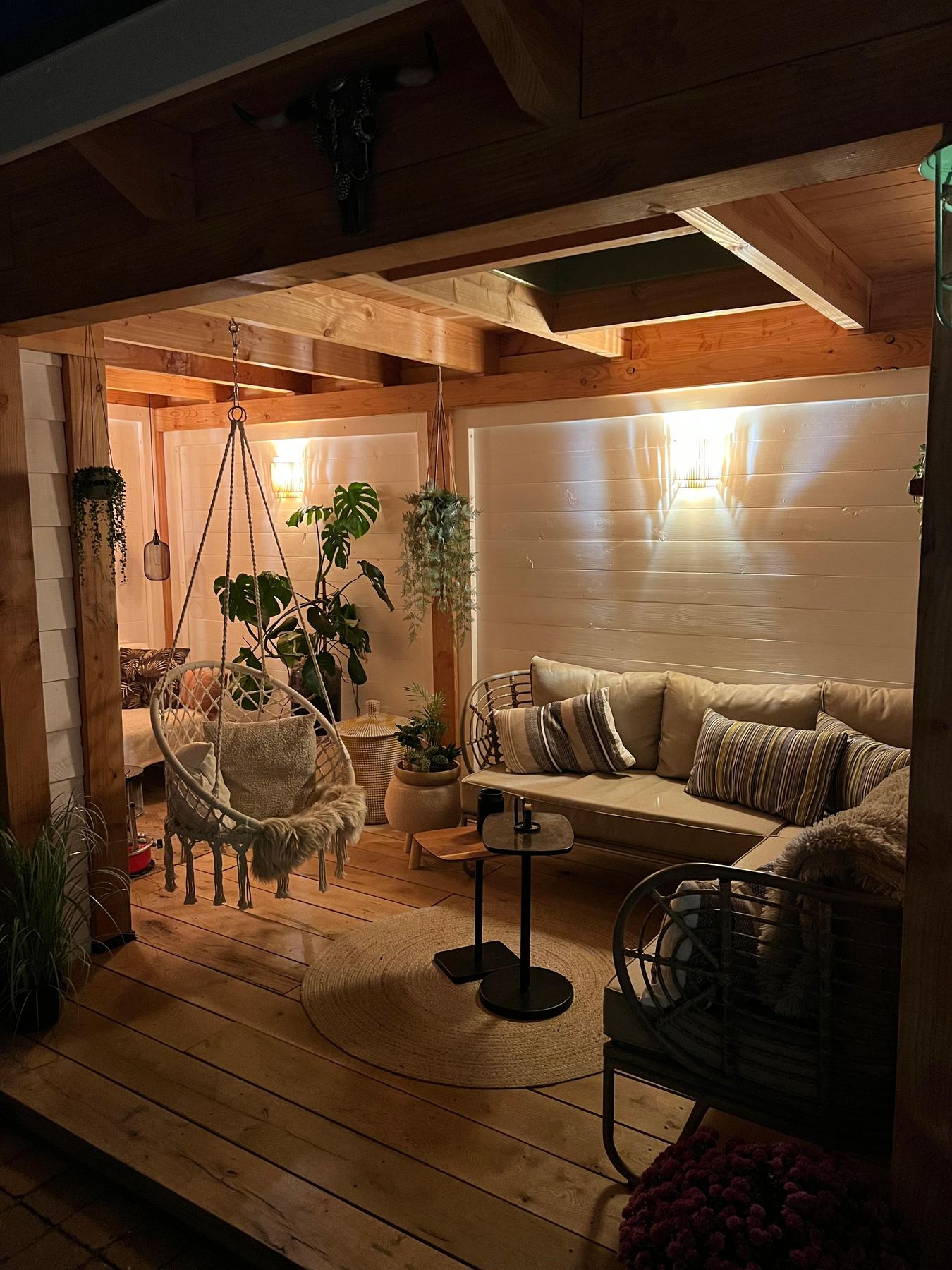 Warm verlichte buitenkamer met loungebank, hangstoel en veel groen