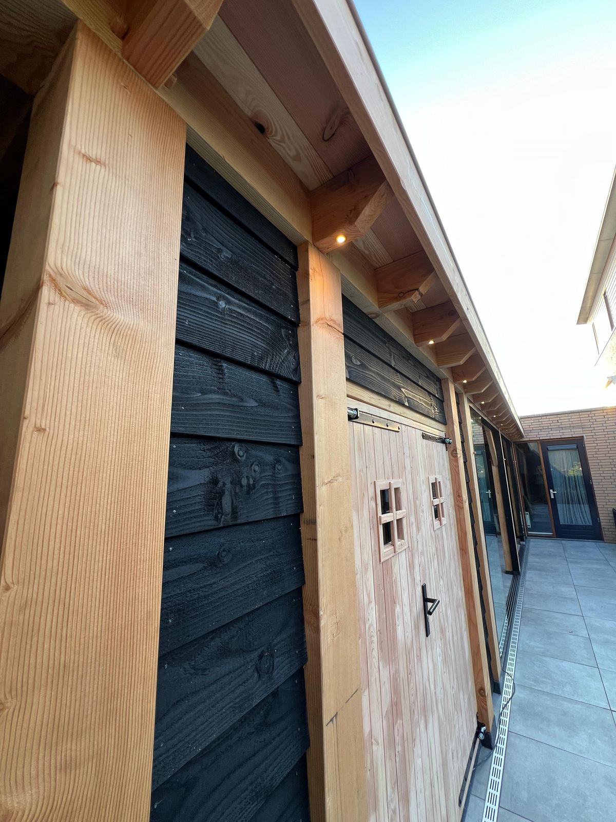 Zwarte gevelwand met bergingsdeuren onder een verlicht dakoverstek