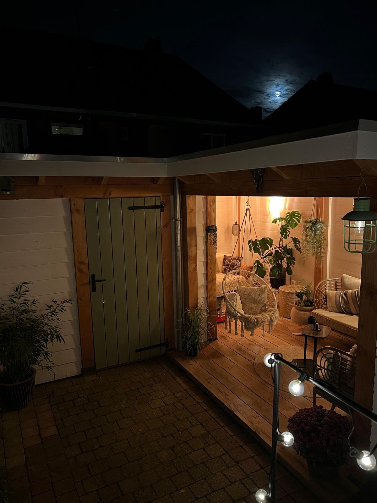 Overdekte entree met houten vlonder en verlichting in de avond