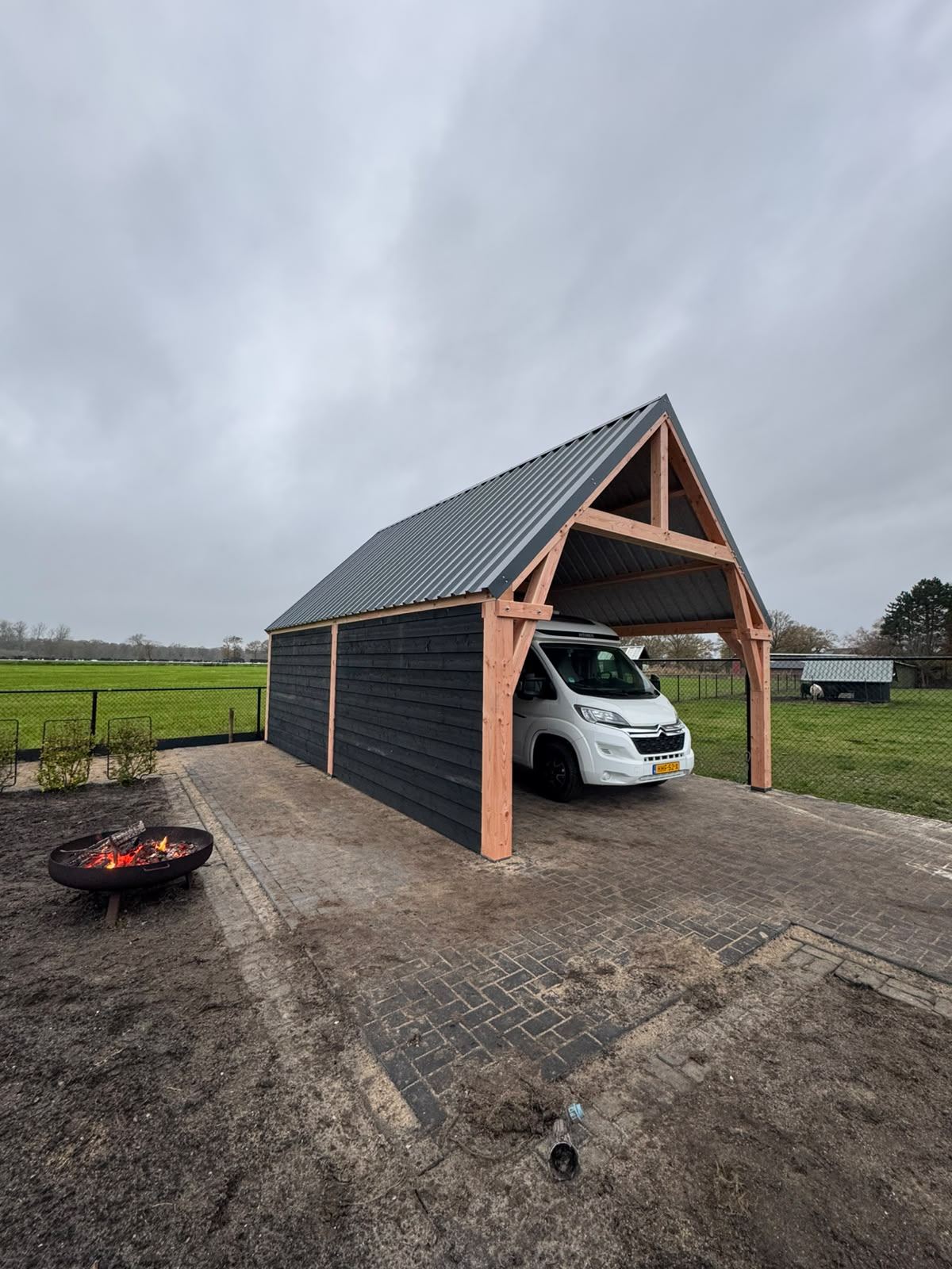 Camper onder een houten overkapping met zadeldak