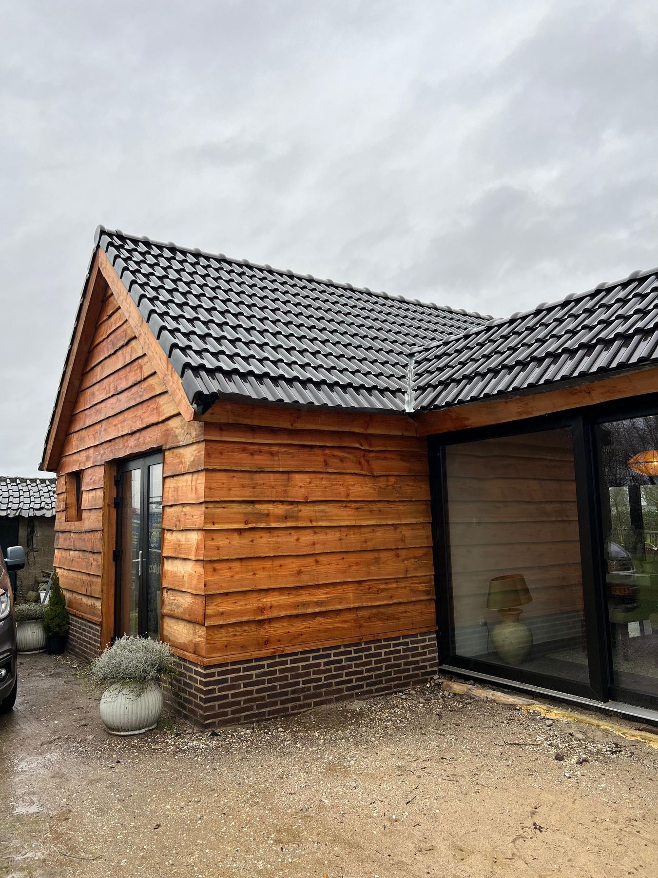 Houten bijgebouw met pannendak en verticale gevelbekleding naast een woning
